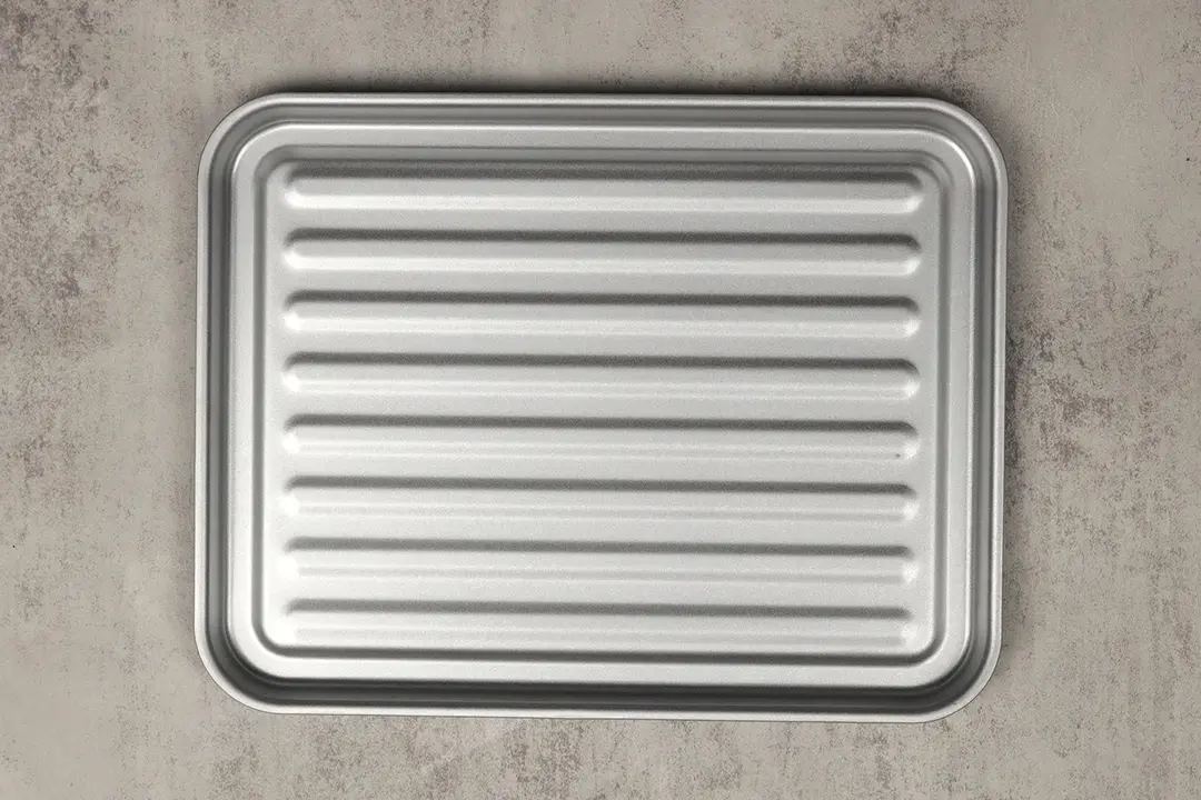 A grooved silver baking pan of the white Comfee CFO-BB101 Compact Countertop Toaster Oven on a grey background.