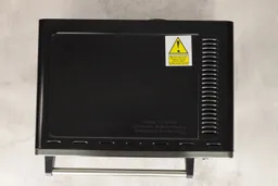 On a grey background, the top of the Toshiba AC25CEW-BS Convection Toaster Oven has air ventilation holes.