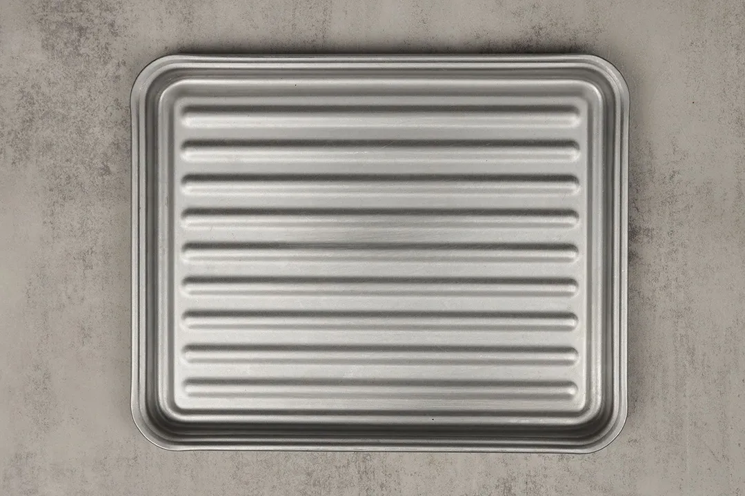 A grooved silver baking pan of the Toshiba AC25CEW-BS Convection Toaster Oven on a grey background.