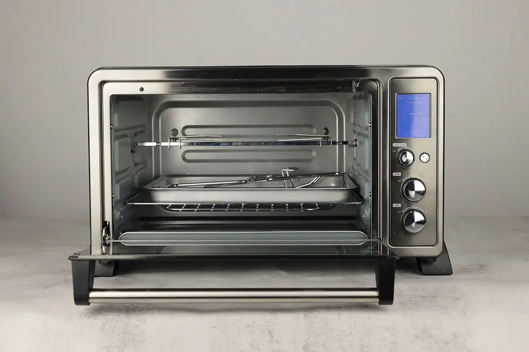 The front of an opened Toshiba AC25CEW-BS with a crumb tray, oven rack, baking pan, lifter, rack clamp, and rotisserie kit.