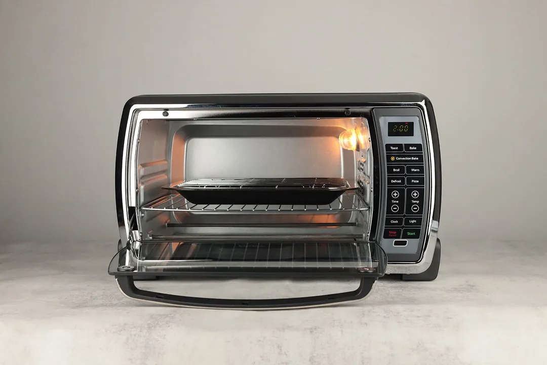 The front of an opened Oster TSSTTVMNDG-SHP-2 Large Convection Toaster Oven with an oven rack, baking pan, and broiling rack.