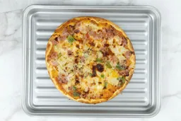 A toaster oven baked 9-inch thick-crust meat pizza with cheese, onions, and green bell peppers on top. The pizza is inside a grooved silver baking pan on a white background.