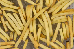 A closeup of pieces of golden baked french fries using a toaster oven inside a stainless steel air fryer basket on a grey background.