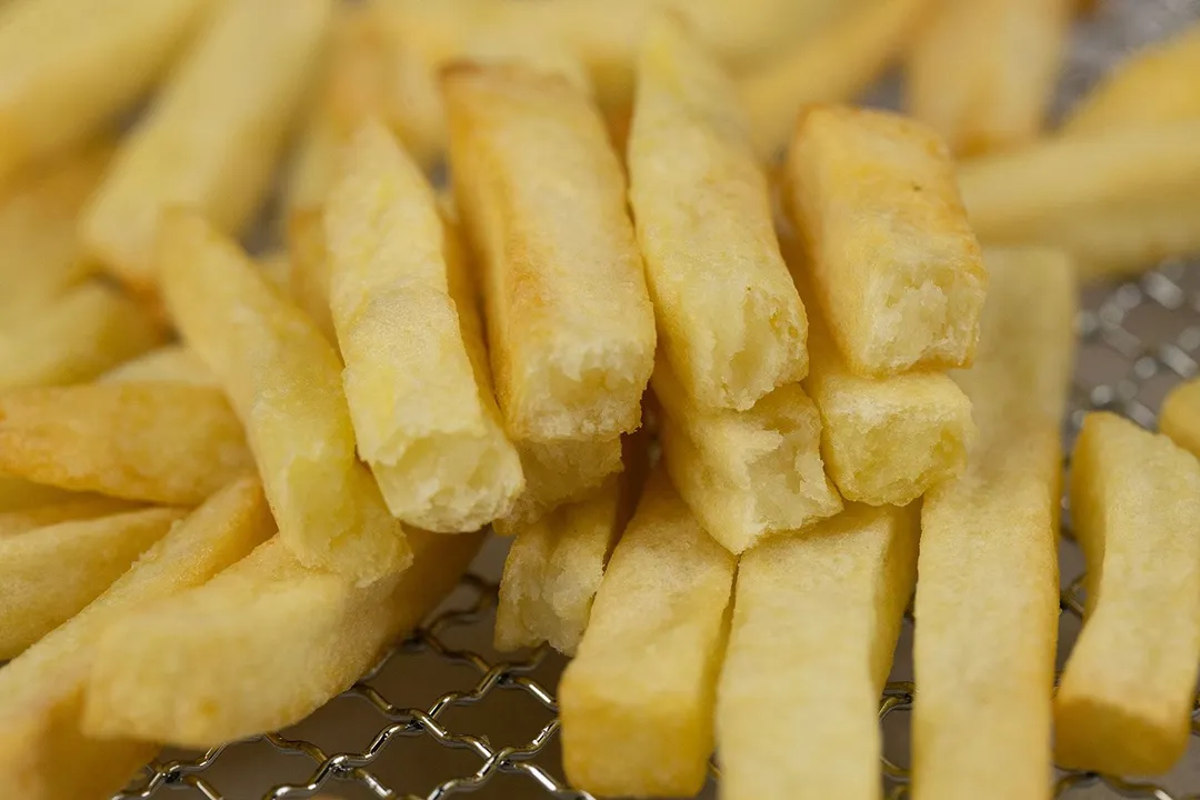 Pieces of golden baked french fries using a toaster oven. Nine pieces of broken-up fries are stacked on top of pieces of whole fries inside an air fryer basket.
