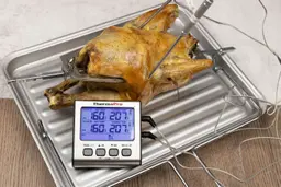 A whole roasted rotisserie chicken on a baking pan. The thermometer has two probes inside the chicken and displays 207°F.