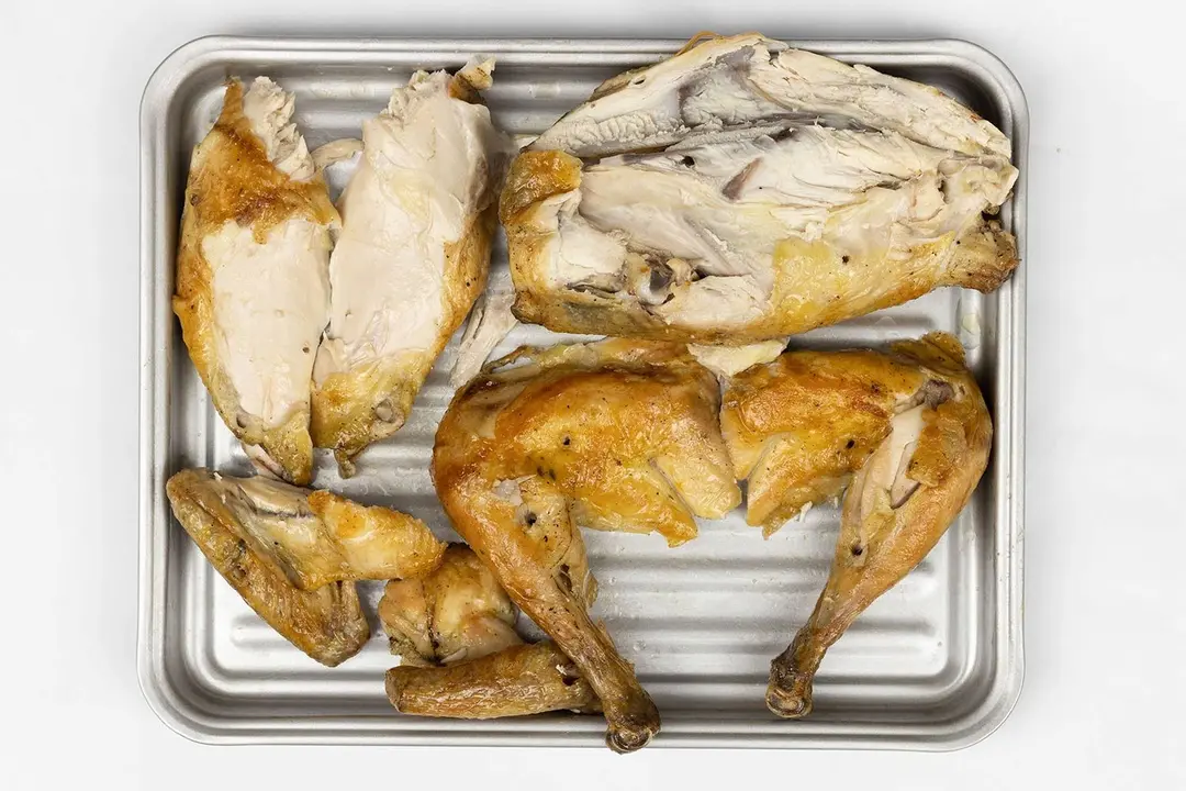 The chicken is carved into seven pieces including a carcass, two breasts, two wings, and two thighs on a silver baking pan.