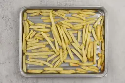 Pieces of golden baked french fries using a toaster oven on a grooved silver baking pan on a grey background.