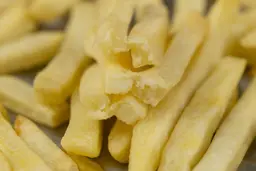 Six pieces of broken-up baked french fries are stacked on top of pieces of whole fries on a grooved silver baking pan.
