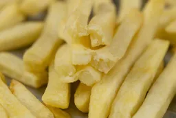Six pieces of broken-up baked french fries are stacked on top of pieces of whole fries on a grooved silver baking pan.