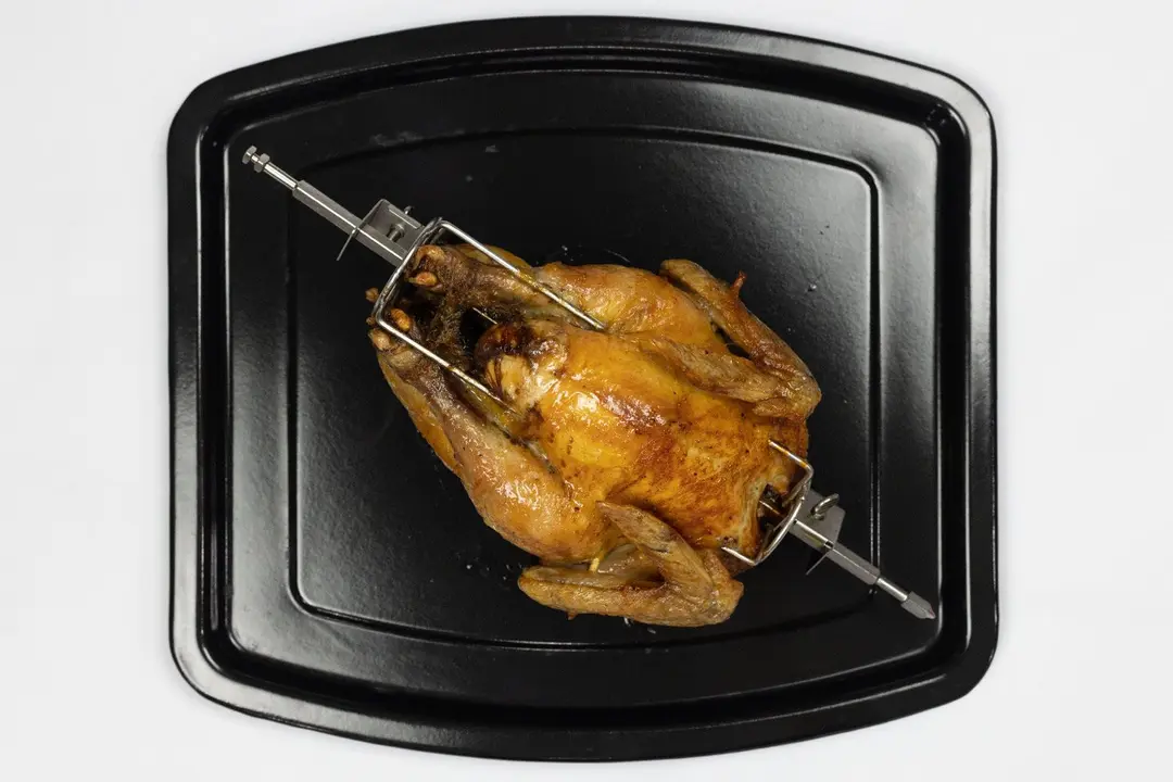 A whole roasted rotisserie chicken using a toaster oven on an enamel baking pan on a white background.