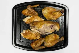 Seven pieces of a carved chicken including a carcass, two breasts, two wings, and two thighs on an enamel baking pan.