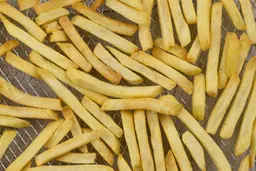A close-up of pieces of baked french fries using a toaster oven inside an air fryer basket on a grey background.