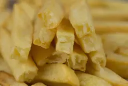 Ten pieces of broken-up baked french fries are stacked on top of pieces of whole fries inside an air fryer basket.