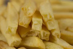 Ten pieces of broken-up baked french fries are stacked on top of pieces of whole fries inside an air fryer basket.