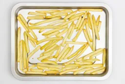 Pieces of baked french fries using a toaster oven on a silver baking pan on a white background.