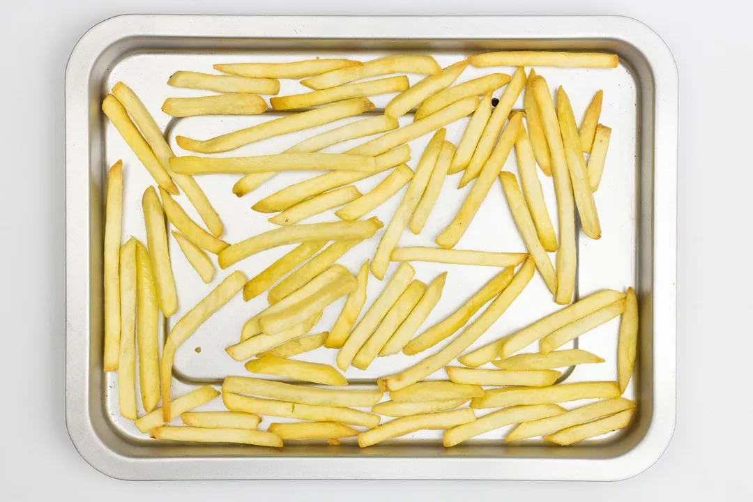 Pieces of baked french fries using a toaster oven on a silver baking pan on a white background.