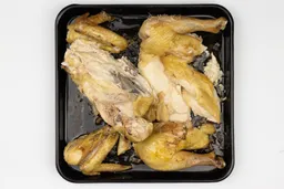 Seven pieces of a carved chicken including a carcass, two breasts, two wings, and two thighs on an enamel baking pan.