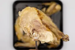 The chicken thigh is slightly pink near the bone. In the white background is the rest of the roasted chicken on a baking pan.