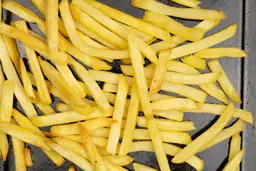 A close-up of pieces of baked french fries using a toaster oven on an enamel baking pan on a white background.