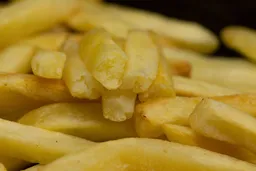 Six pieces of broken-up baked french fries are stacked on top of pieces of whole fries on an enamel baking pan.