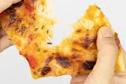 Two hands break apart a slice of pizza with melty cheese, meat, and green bell peppers on top baked using a toaster oven.