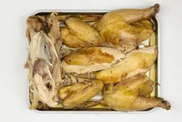 Seven pieces of a carved chicken including a carcass, two breasts, two wings, and two thighs on a silver baking pan.