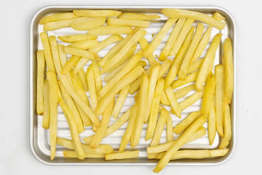 Pieces of baked french fries using the Comfee CFO-BB101 Toaster Oven on a grooved silver baking pan on a white background.