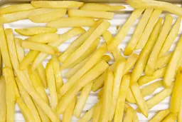 A close-up of pieces of baked french fries using the Comfee CFO-BB101 on a grooved silver baking pan on a white background.