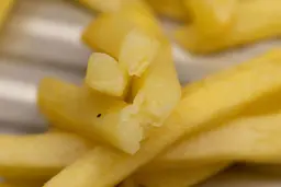 Four pieces of broken-up baked french fries are stacked on top of pieces of whole fries on a grooved silver baking pan.