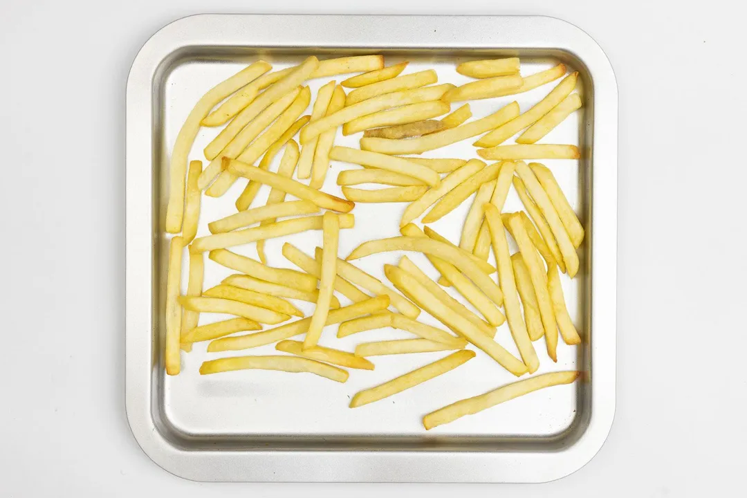 Pieces of baked french fries using the Cuisinart TOB-40N Toaster Oven Broiler on a silver baking pan on a white background.