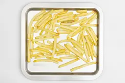 Pieces of baked french fries using the Cuisinart TOB-40N Toaster Oven Broiler on a silver baking pan on a white background.
