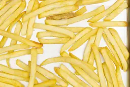 A close-up of pieces of baked french fries using the Cuisinart TOB-40N Oven on a silver baking pan on a white background.