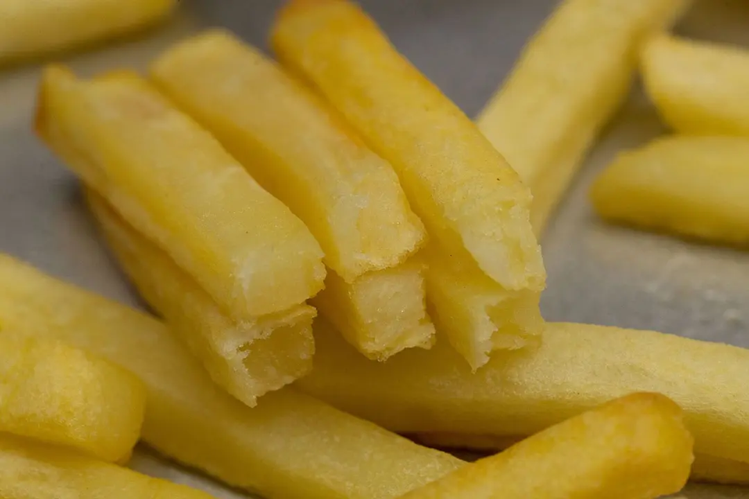 Six pieces of broken-up baked french fries are stacked on top of pieces of whole fries on a silver baking pan.