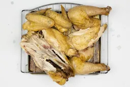 Seven pieces of a carved chicken including a carcass, two breasts, two wings, and two thighs on a silver baking pan.