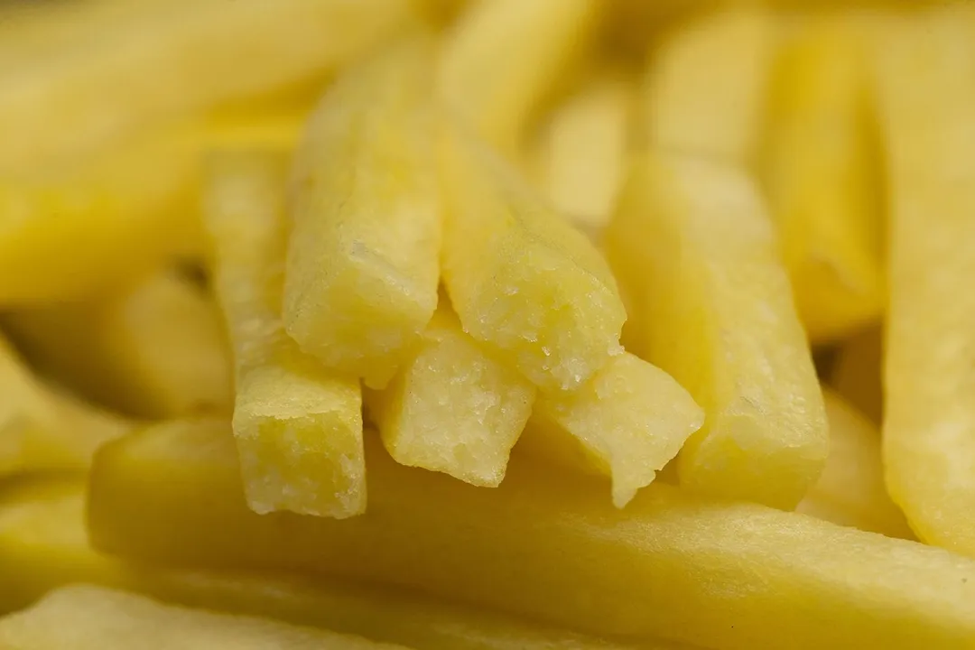 Six pieces of broken-up baked french fries are stacked on top of pieces of whole fries on a silver baking pan.