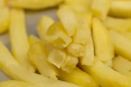 Eight pieces of broken-up baked french fries are stacked on top of pieces of whole fries on a silver baking pan.
