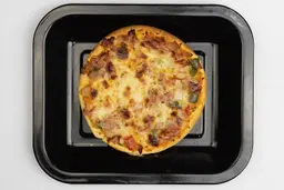 A toaster oven baked 9-inch thick-crust meat pizza with cheese, onions, and green bell peppers on top inside a baking pan.