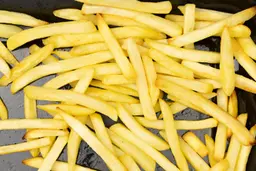 A close-up of pieces of baked french fries using the Oster TSSTTVMNDG-SHP-2 on an enamel baking pan on a white background.