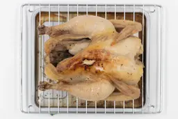 A whole roasted chicken using the Black+Decker TO1760SS belly up on an oven rack and baking pan on a white background.