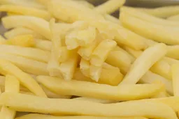 Ten pieces of broken-up baked french fries are stacked on top of pieces of whole fries on a silver baking pan.