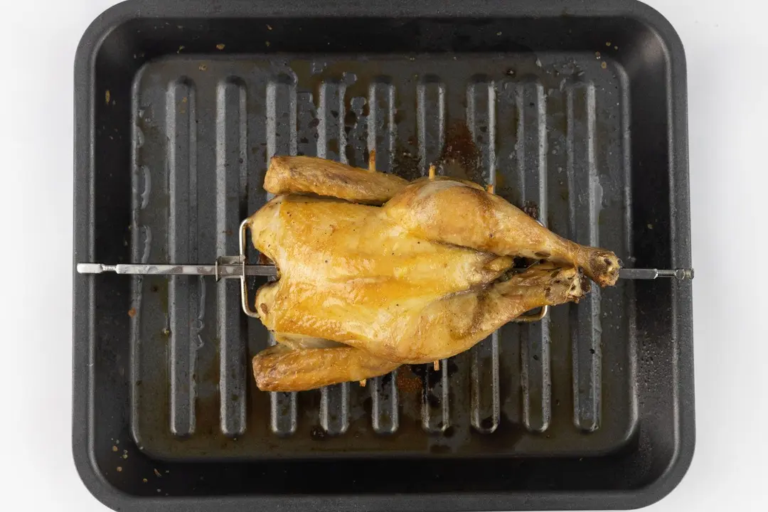 A whole roasted rotisserie chicken using the Cosori CO130-AO Oven belly up on a grey baking pan on a white background.