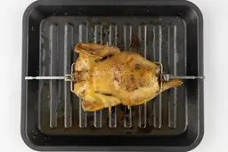A whole roasted rotisserie chicken using the Cosori CO130-AO Oven backside up on a grey baking pan on a white background.