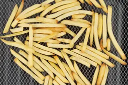 A close-up of pieces of baked french fries using the Cosori CO130-AO inside an air fryer basket on a grey baking pan.