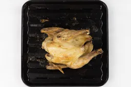 A whole roasted chicken using the Breville BOV845BSSUSC Toaster Oven belly up on an enamel broiling rack and baking pan.