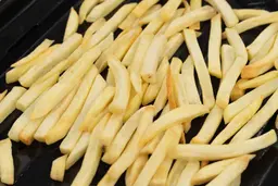 A close-up of pieces of baked french fries using the Breville BOV845BSSUSC on an enamel baking pan on a white background.