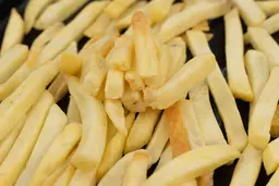 Eight pieces of broken-up baked french fries are stacked on top of pieces of whole fries on an enamel baking pan.