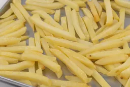 A close-up of pieces of baked french fries using the Hamilton Beach 31344DA on a silver baking pan on a white background.