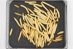 Pieces of baked french fries using the Ninja DT201 Oven inside an air fryer basket and baking pan on a white background.