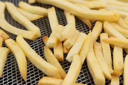 Four pieces of broken-up baked french fries are stacked on top of pieces of whole fries inside an air fryer basket.