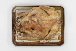 A whole roasted chicken using the Mueller MT-175 Toaster Oven backside up on a silver baking pan on a white background.